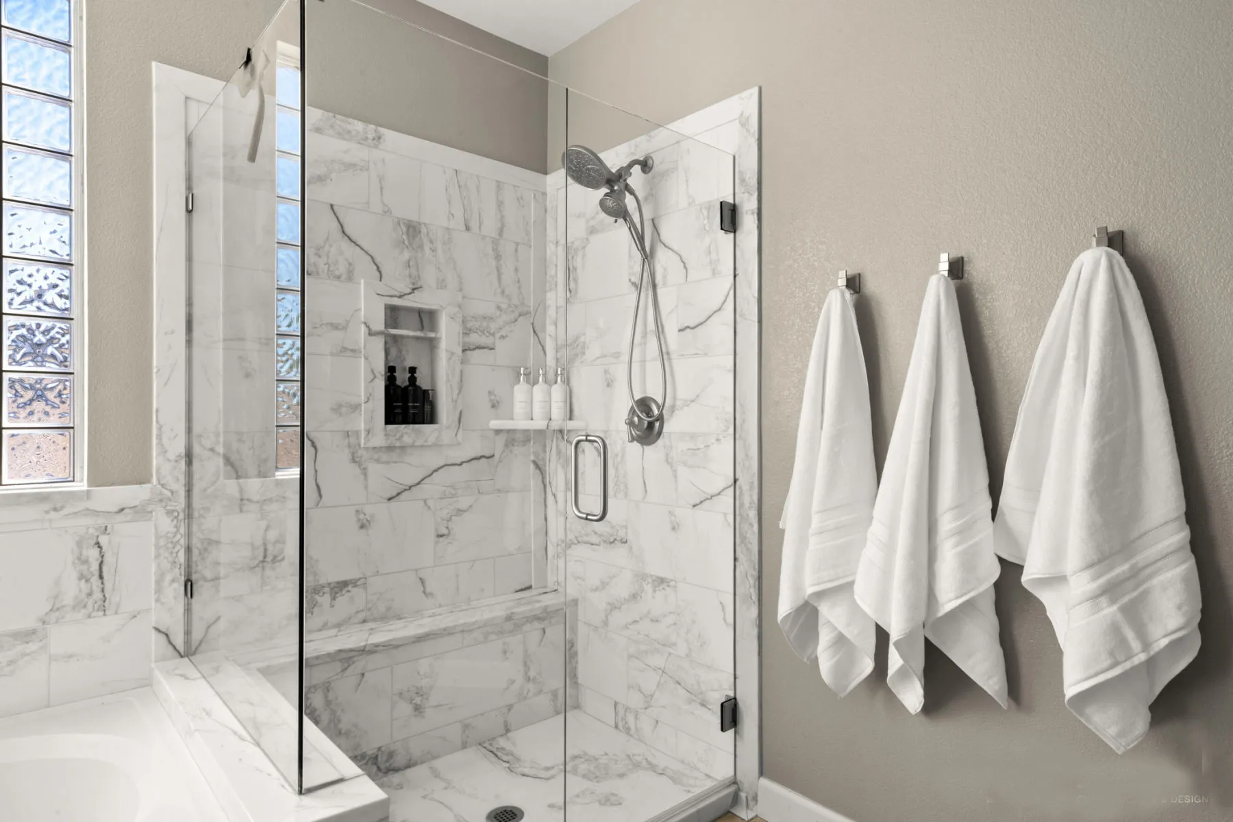 Marble-tiled shower beside the soaking tub and towel hooks