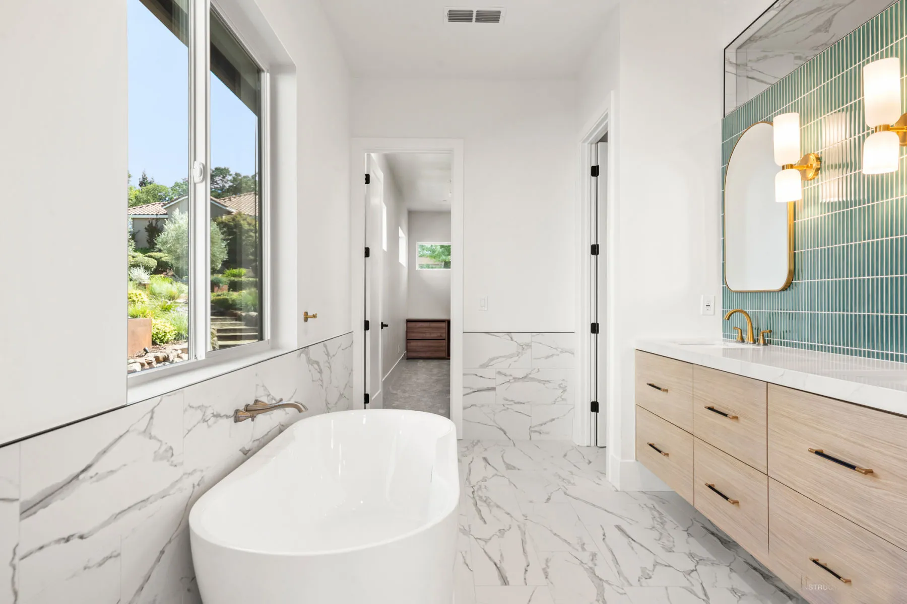 View past the freestanding tub toward the oak vanity and green tile wall