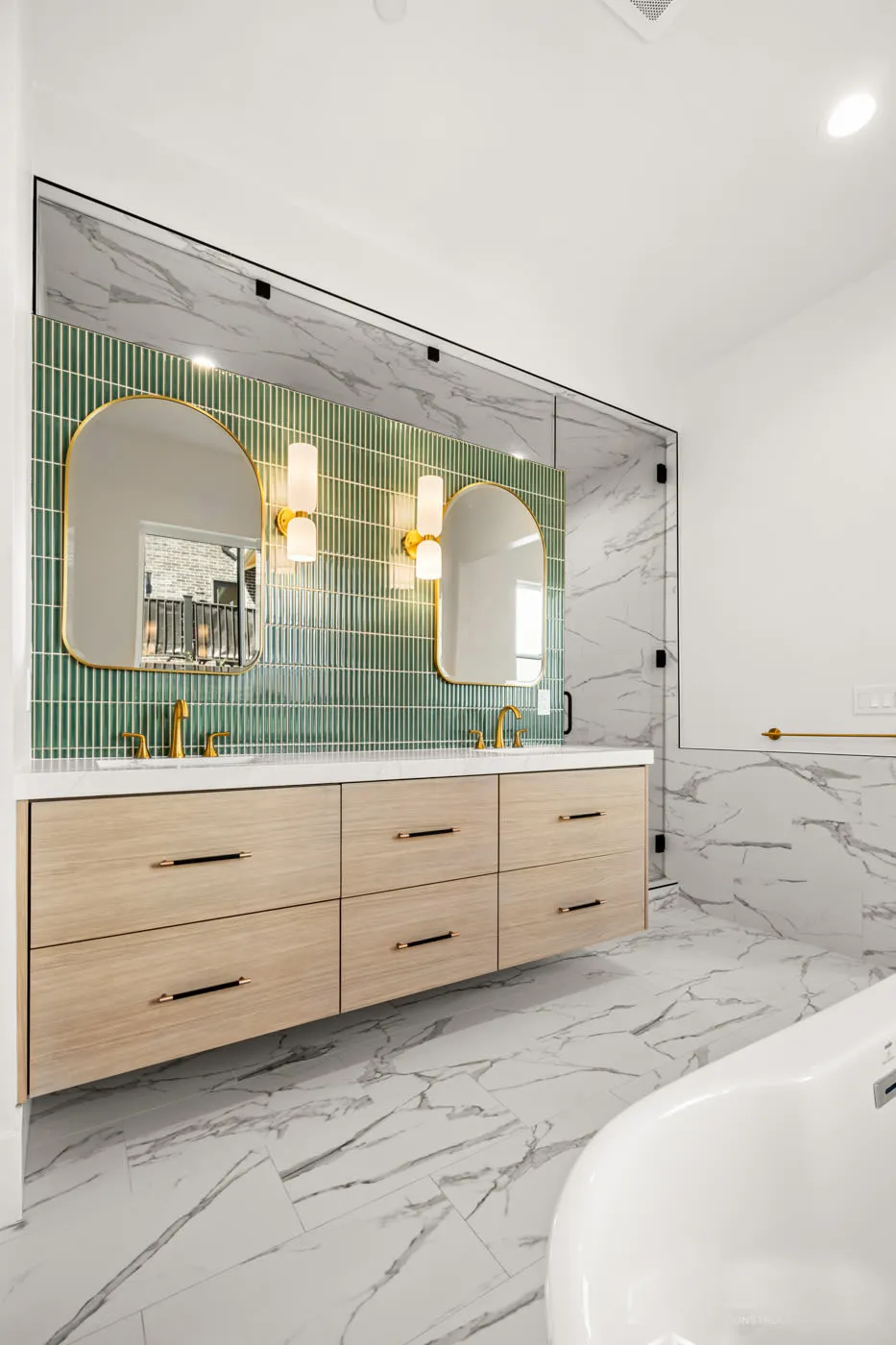 Oak bathroom vanity with arched mirrors, green tile, and a freestanding tub