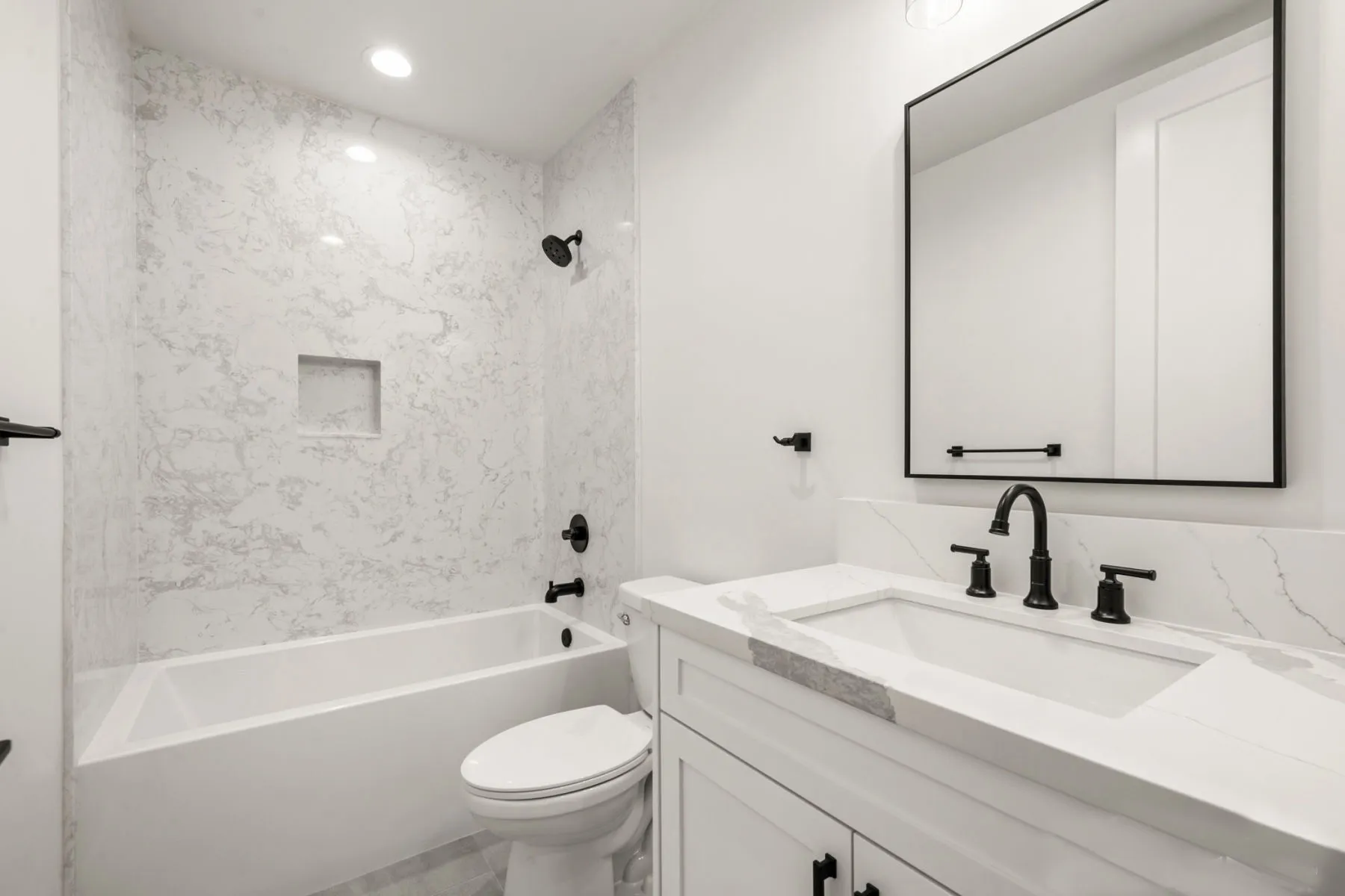 Compact white bathroom with a tub, vanity, and black fixtures