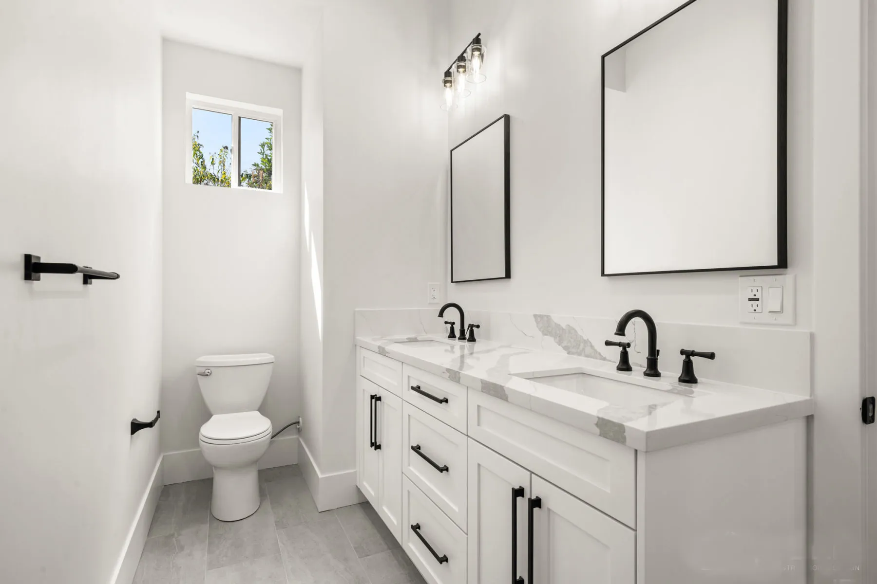 White double vanity with black fixtures and two framed mirrors