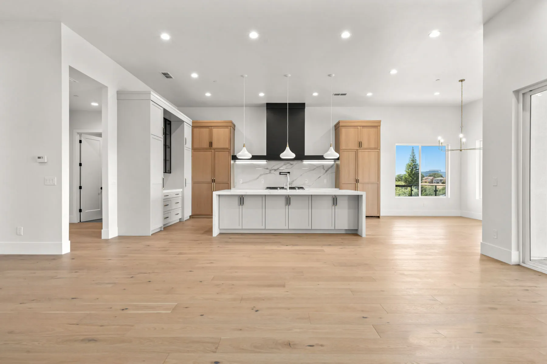 Wide kitchen with a white island, natural oak cabinetry, and a black range hood