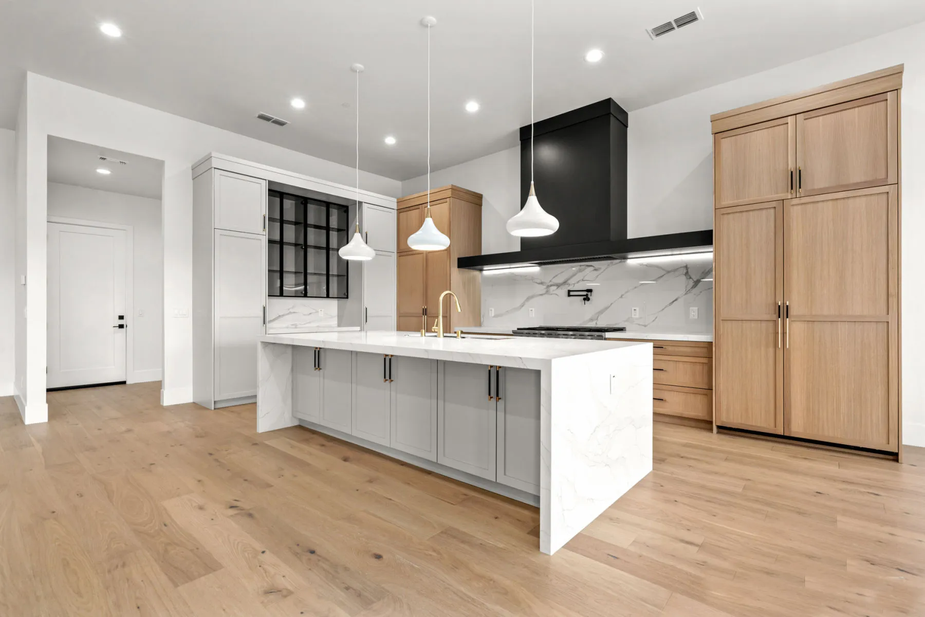 Angled view across the white island toward oak cabinetry and a black range hood