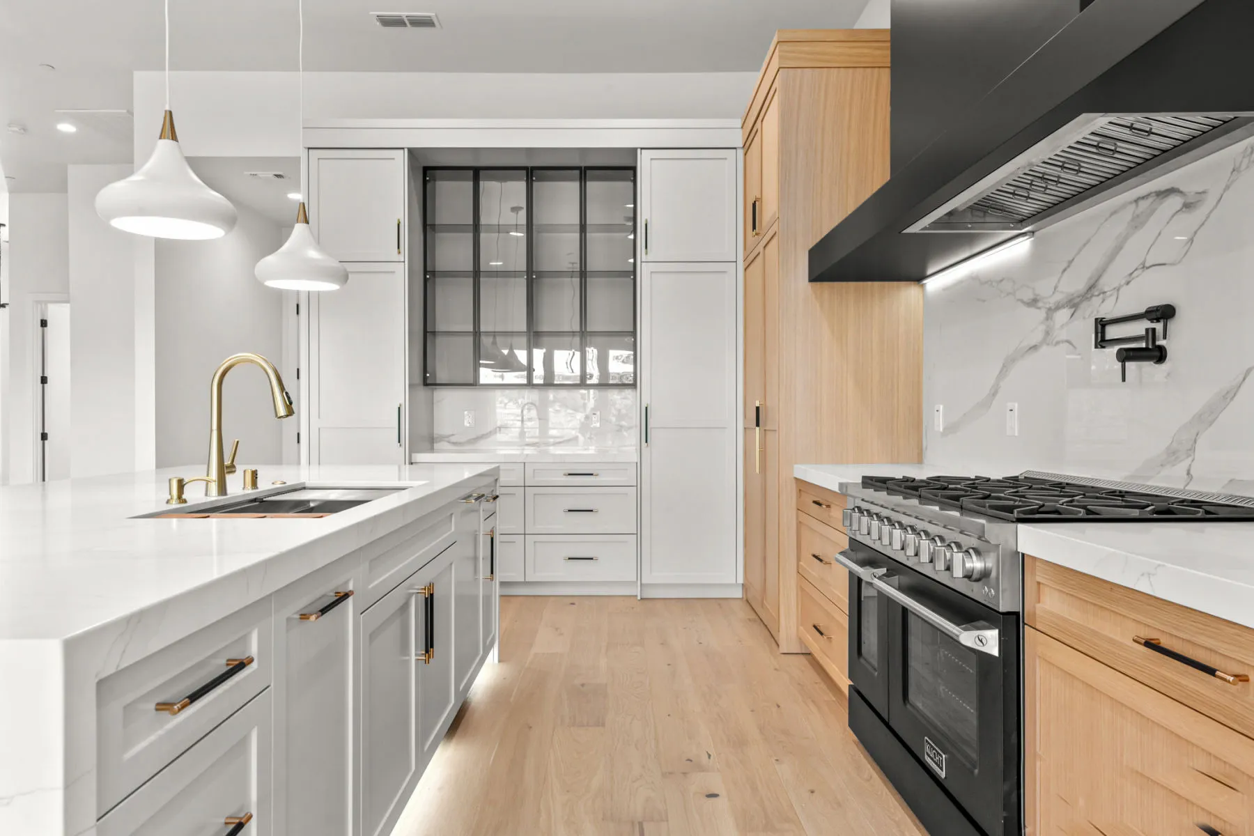 View along the island toward the range, marble backsplash, and tall oak cabinets