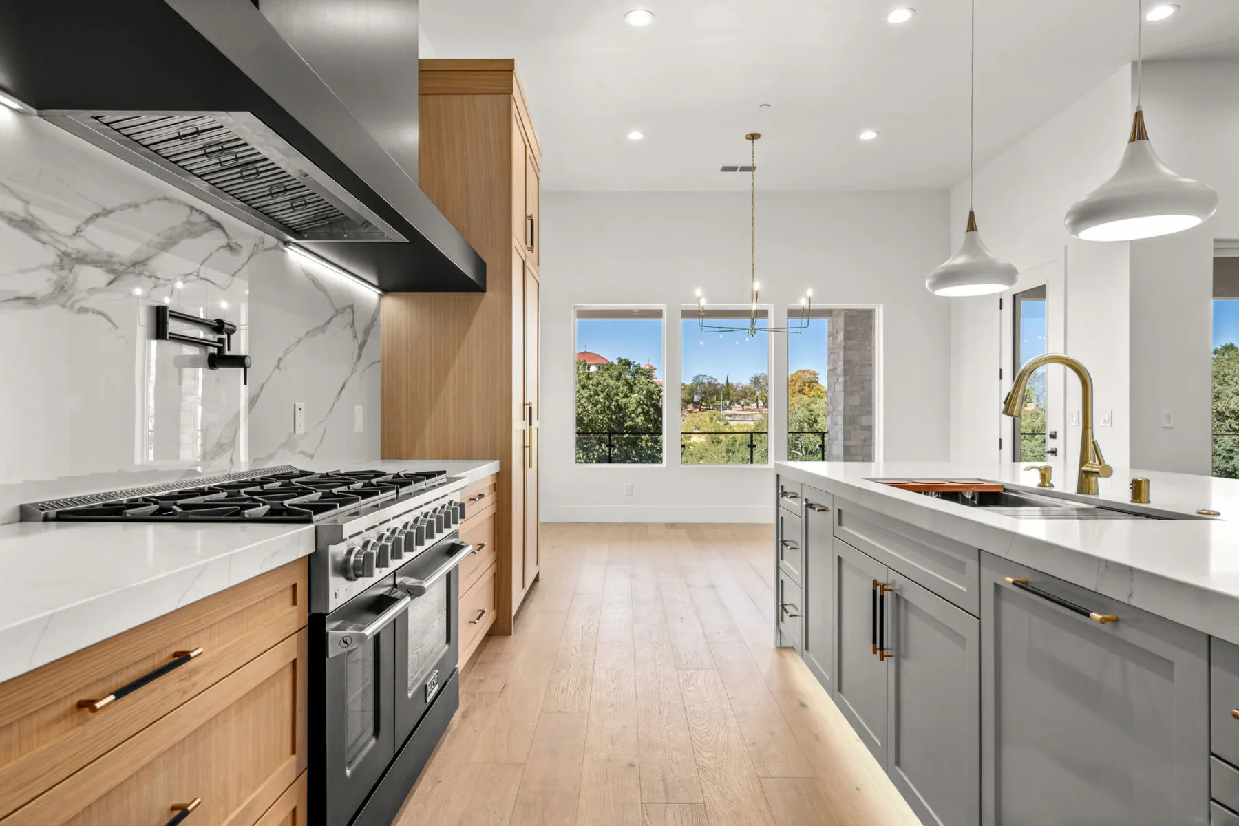 Range wall with black hood, marble backsplash, oak lower cabinets, and pendant lights