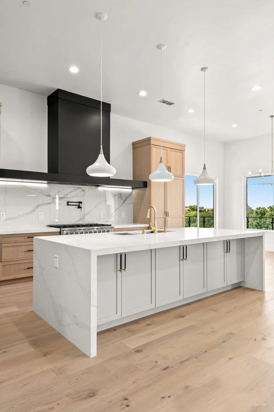 White kitchen island with natural oak cabinetry, marble surfaces, and pendant lighting